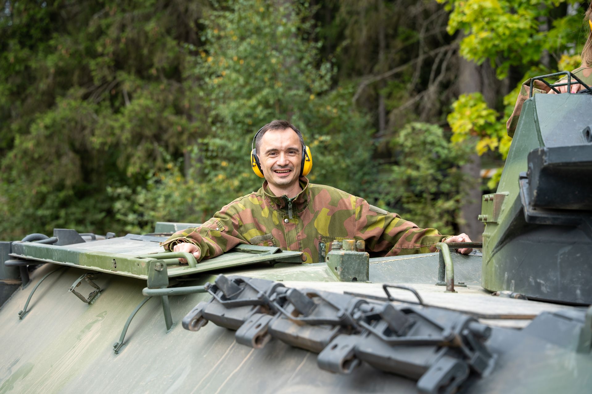 A guest in camouflage overalls looking out of a tank hatch