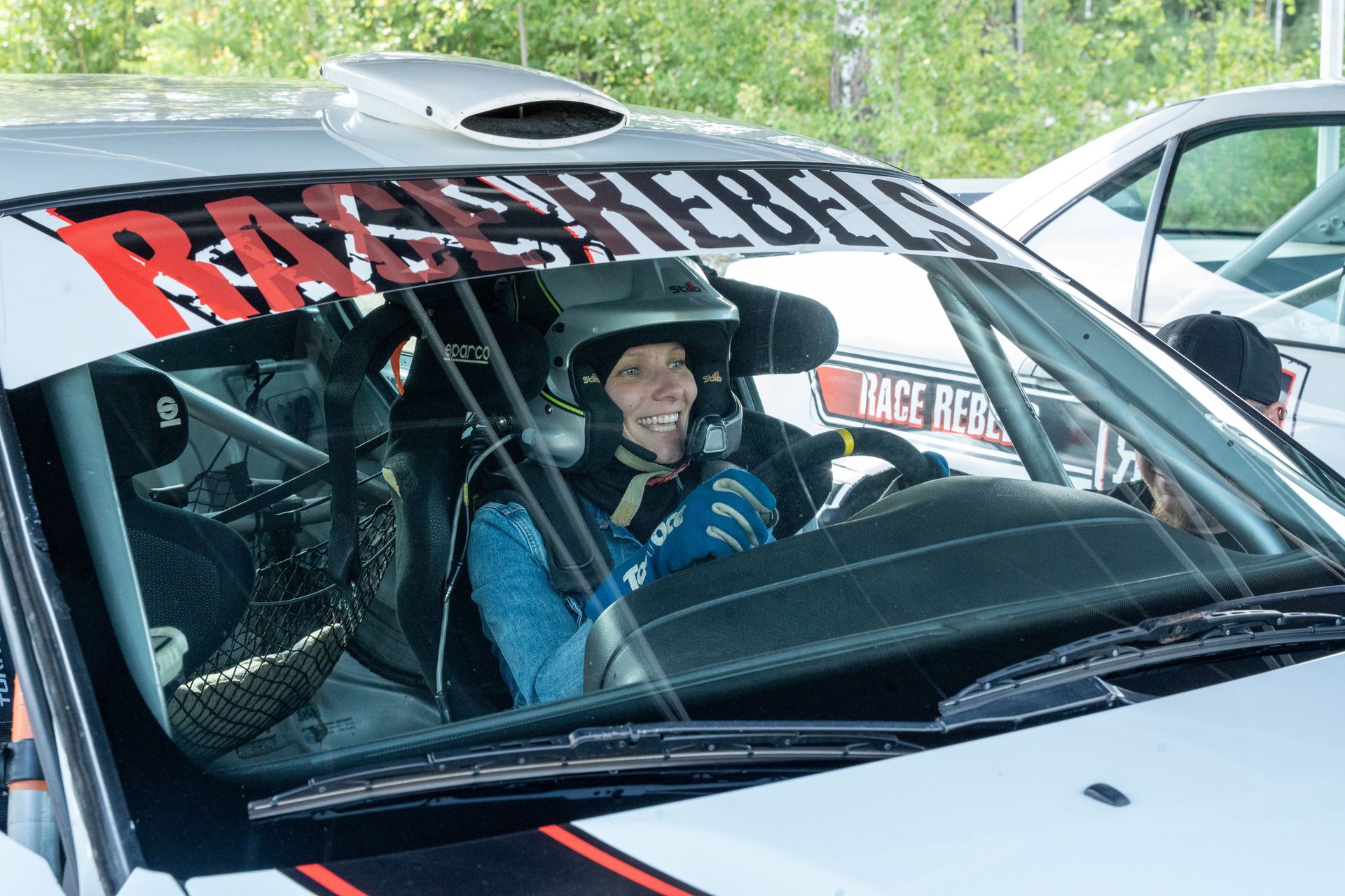A guest smiling from the cockpit of a rally car