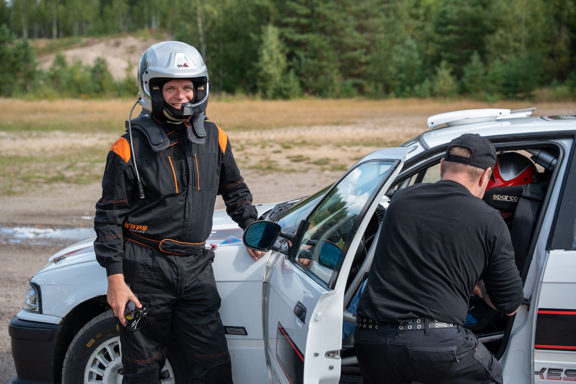A guest in a racing suit beside a rally car with an instructor